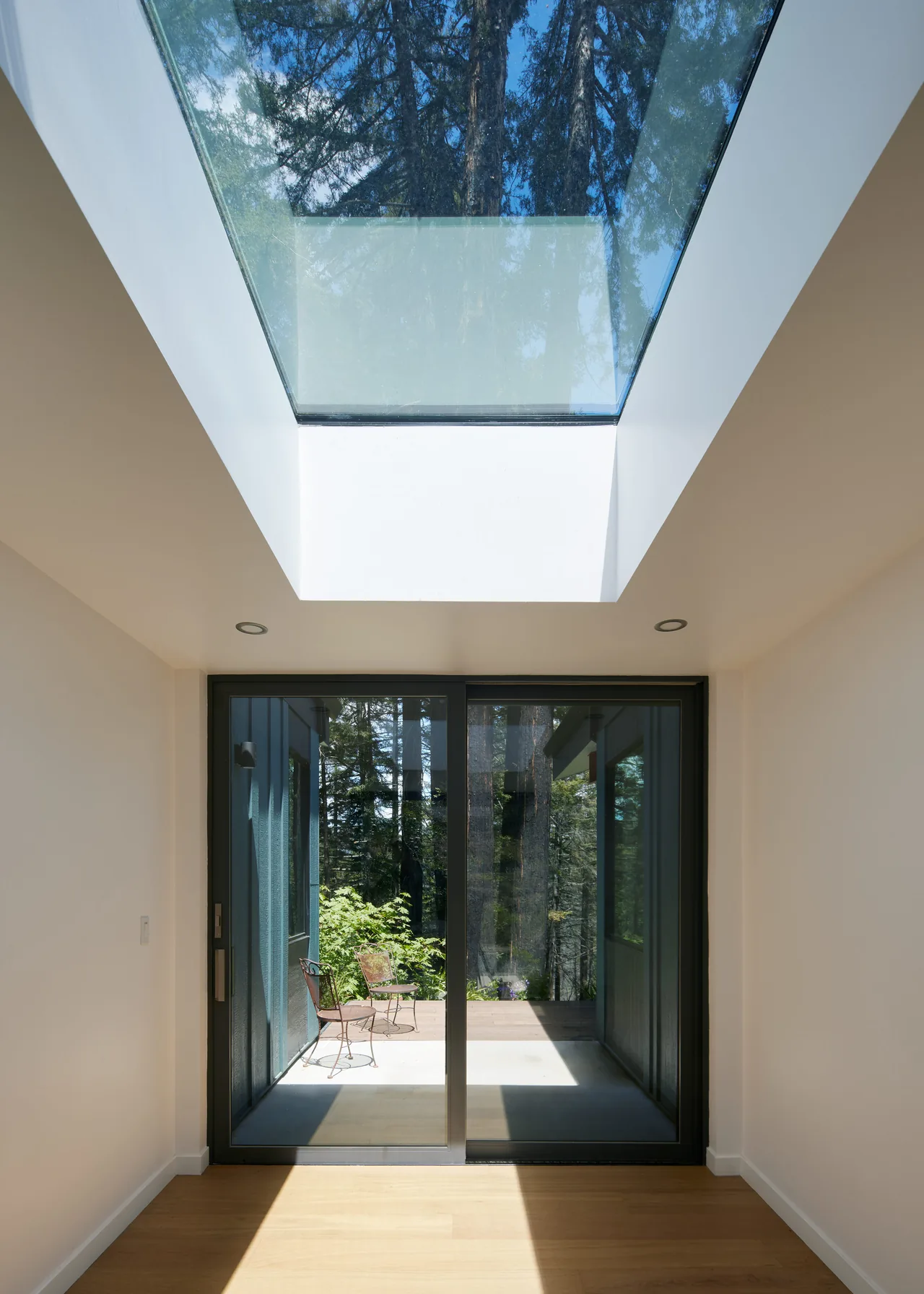 Room with skylight above and black sliding glass doors opening to deck with outdoor metal chairs.