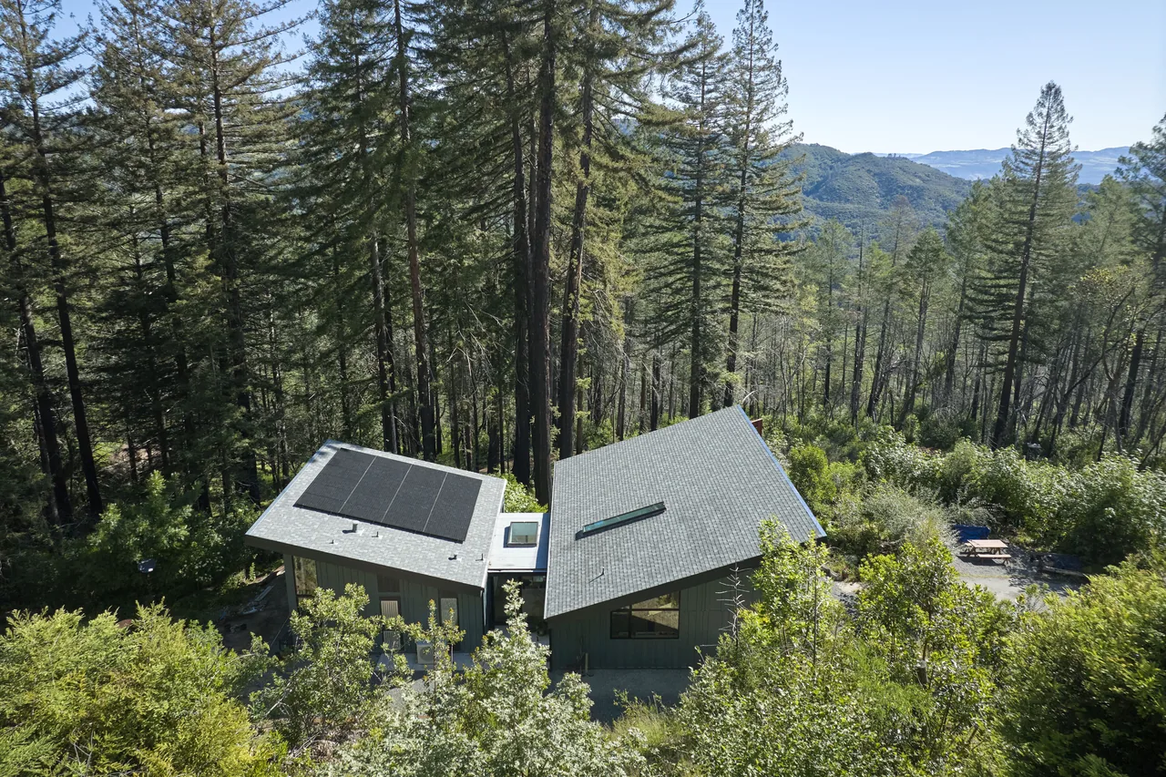 The Butterfly House features two sloped roof sections forming a butterfly roof, situated in a wooded hillside location.