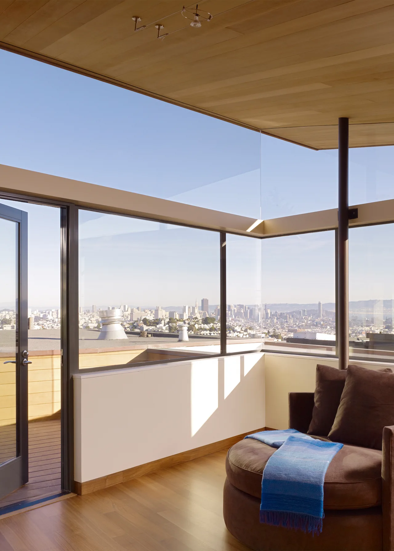 Living room corner with floor-to-ceiling glazing and a black window frame overlooking an urban cityscape.