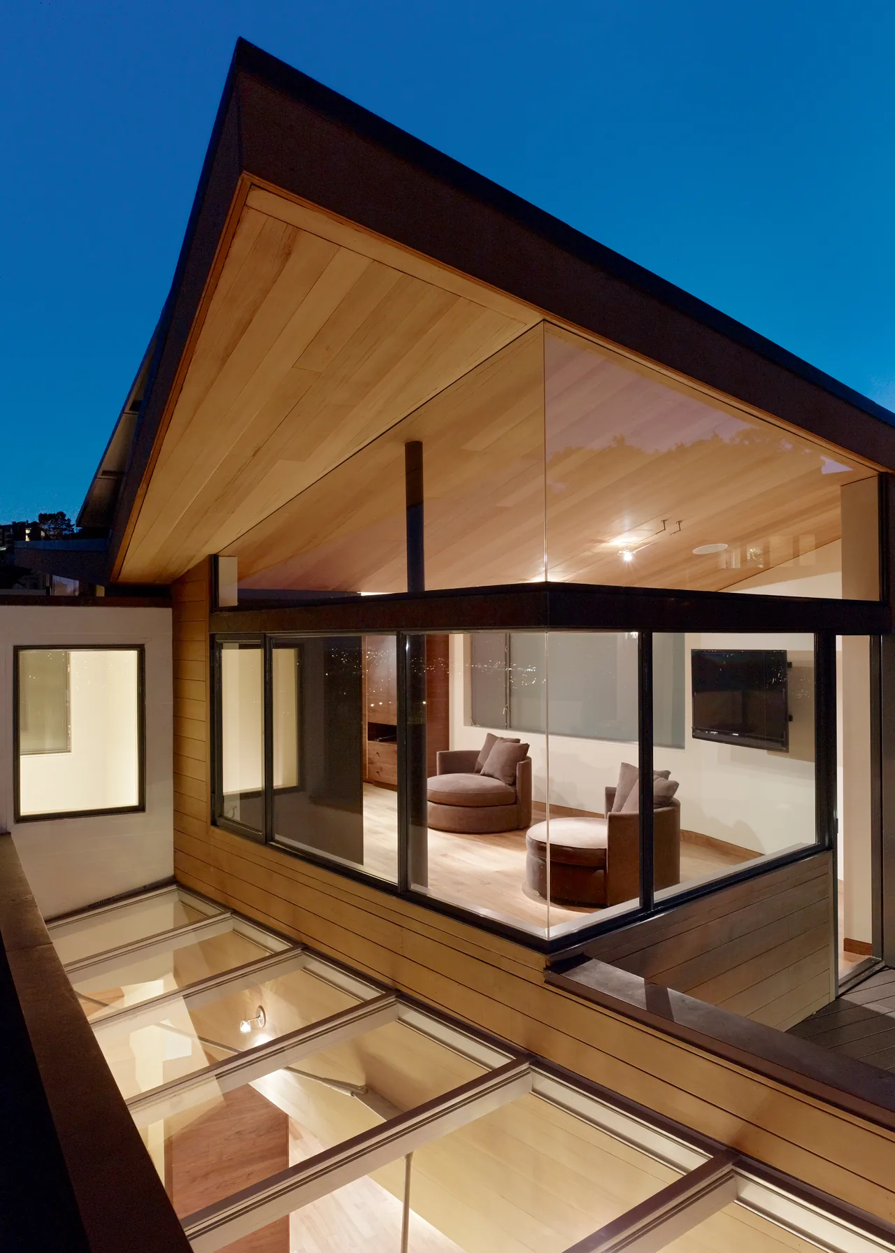 The Vessel by Kennerly Architecture features an exterior wood ceiling and expansive glass windows at dusk.