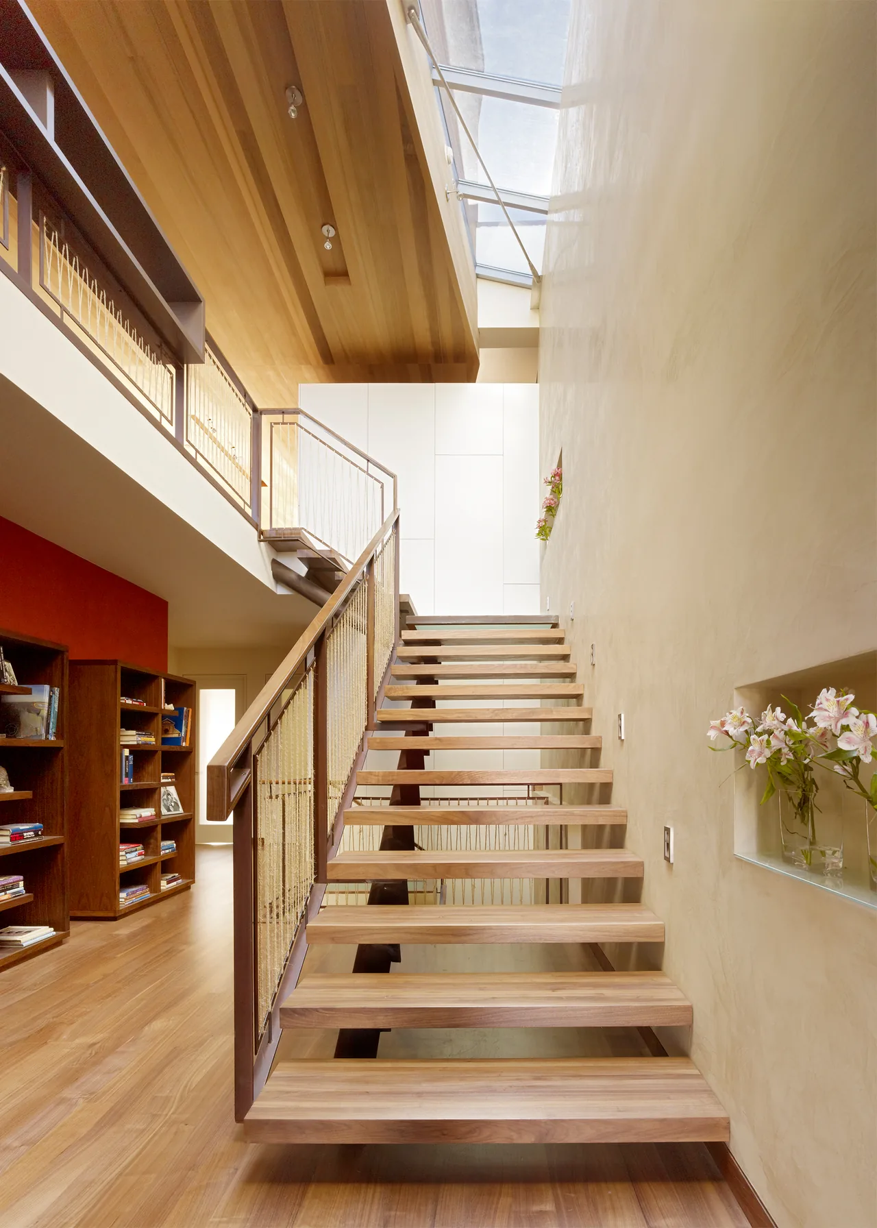 Open floating wood stairs with rope railing lead to an upper floor under a wood-paneled ceiling and glass skylight.