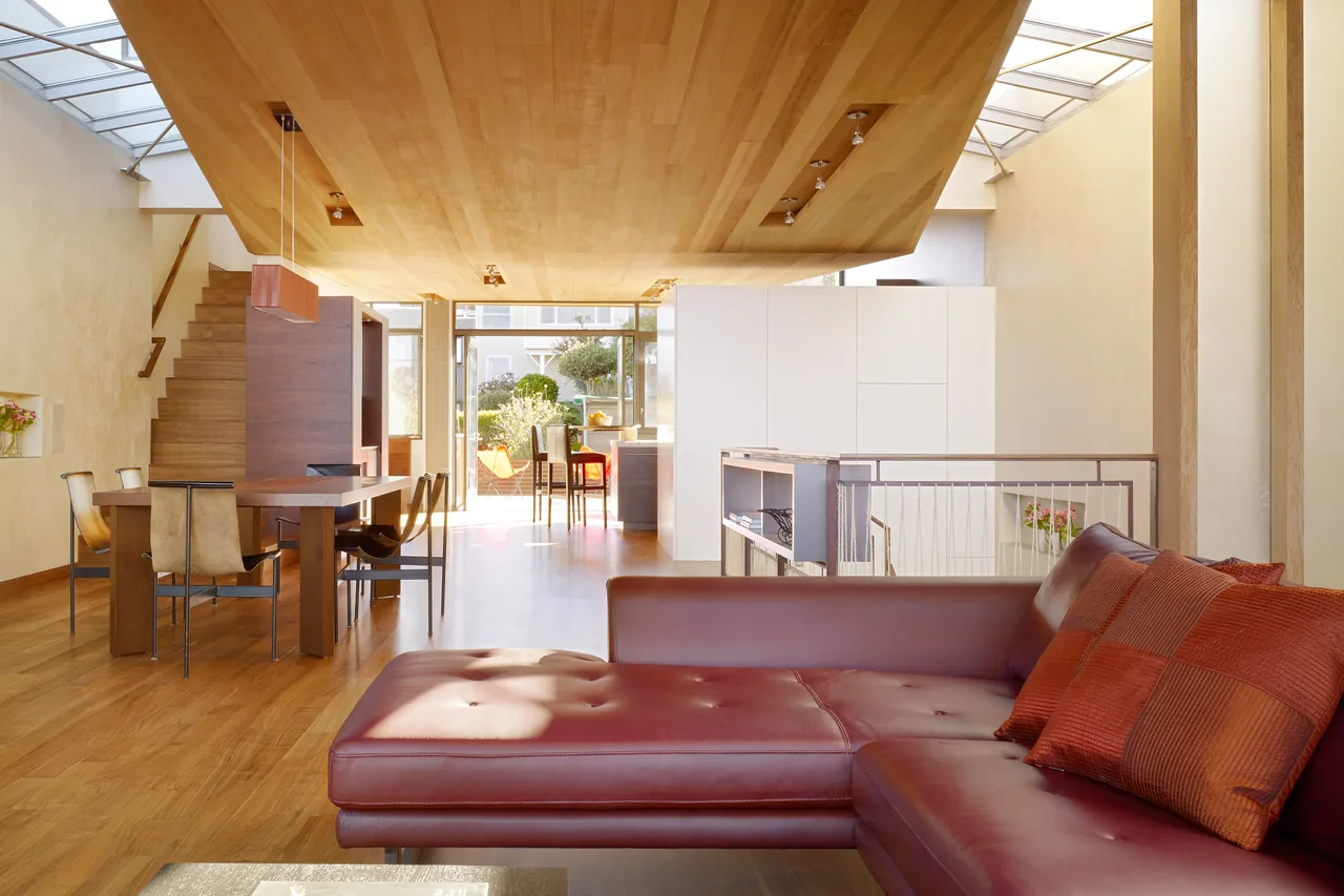 Daylight fills a multi-level living and dining space featuring a leather sofa and wooden finishes in The Vessel project.