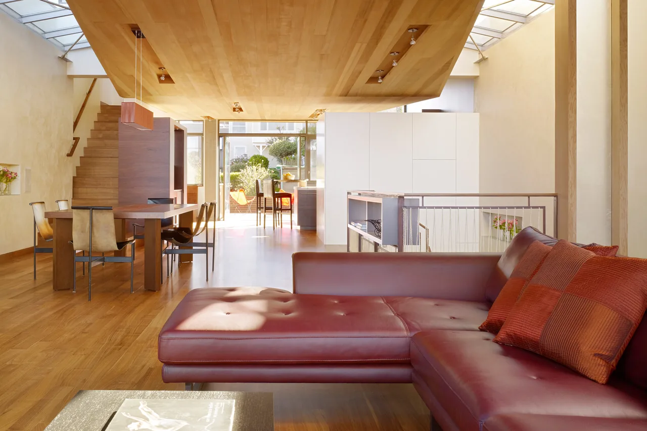 Open living and dining room with skylights, wood ceiling, and leather sectional sofa, leading to glass patio doors.