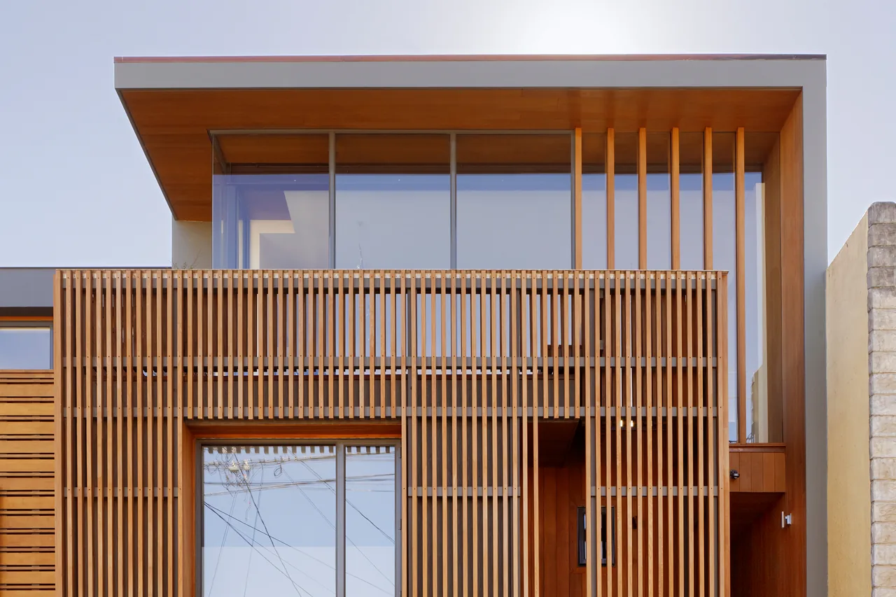 Modern residential facade with large glass windows and vertical wooden slats covering part of the exterior.