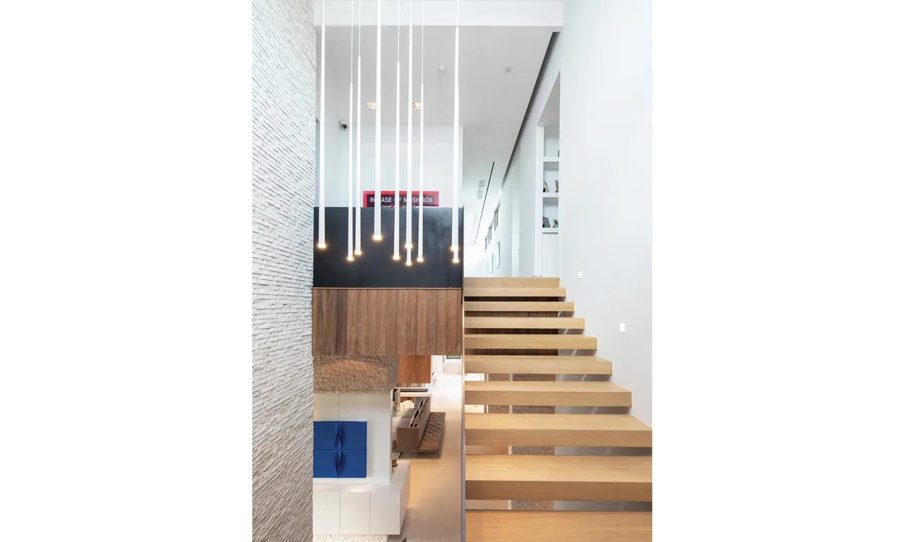 Floating wooden staircase alongside stone wall with pendant lighting in a modern interior.