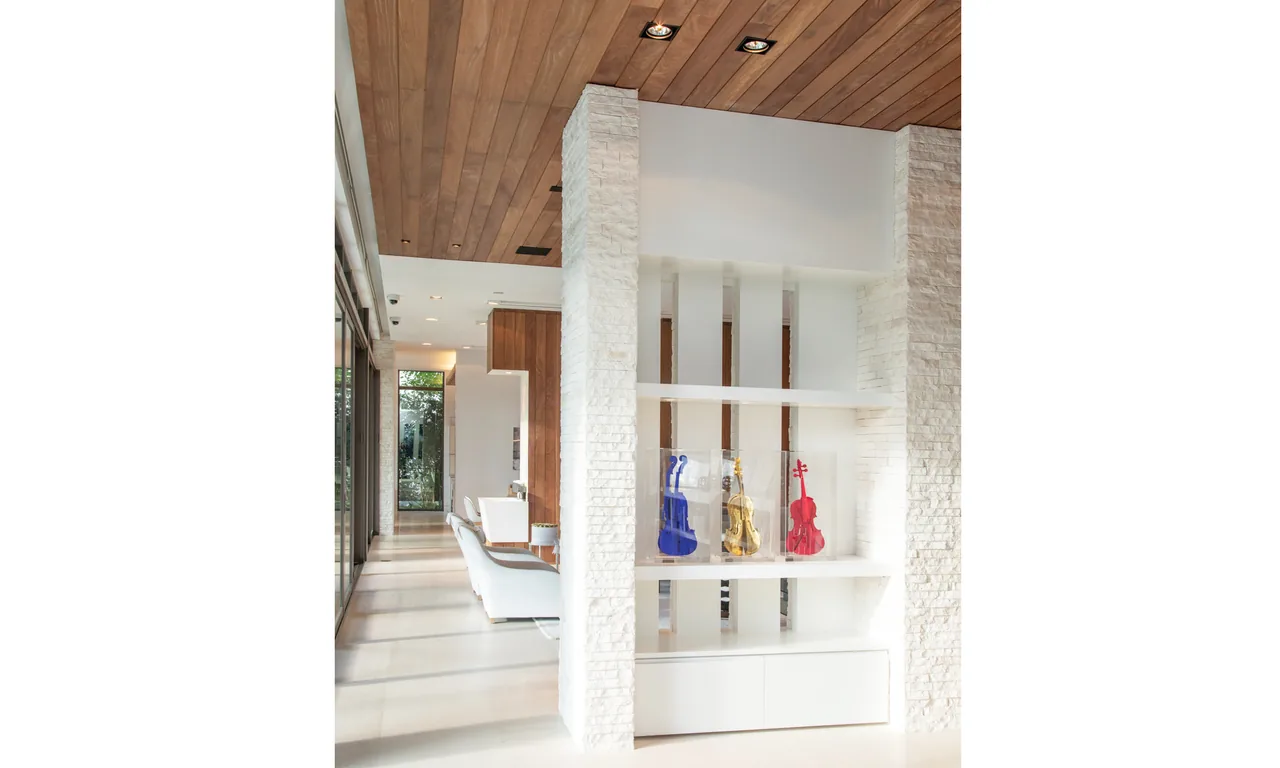 Dining room with wooden ceiling, white stone partition wall, and decorative violins on built-in shelves.