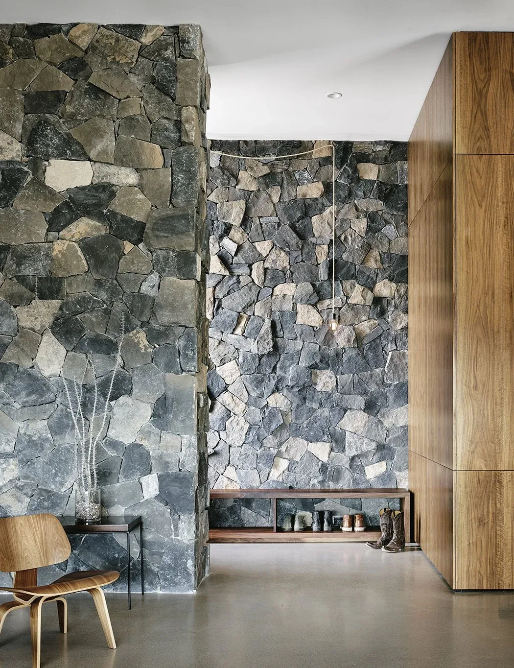 Entryway featuring gray stone walls, wood paneling, and polished concrete flooring with a small built-in shoe shelf.