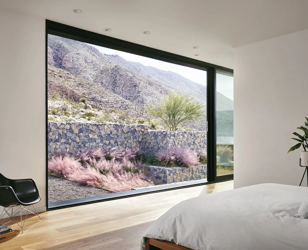 Bedroom features large floor-to-ceiling glazing framing a desert mountain view with stone wall landscaping.