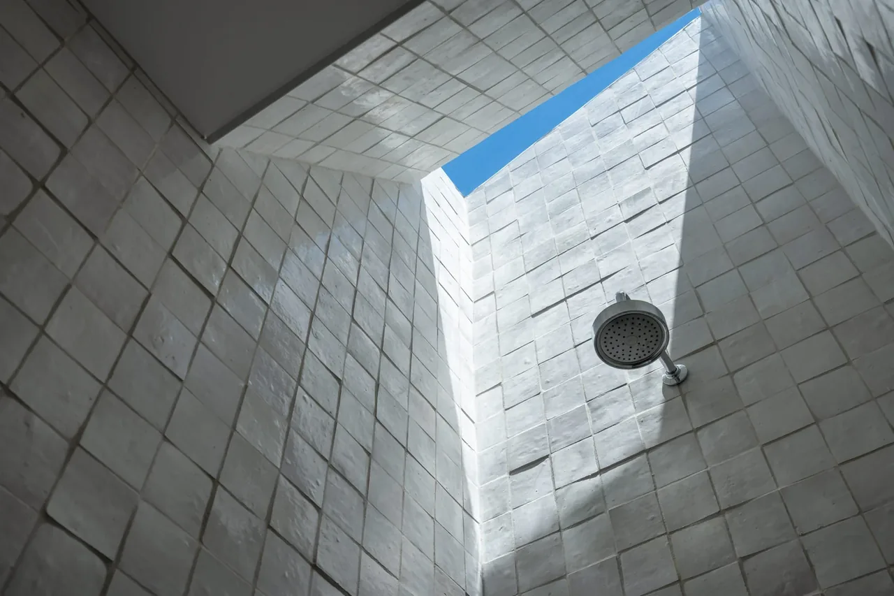 Outdoor shower with white textured tile walls and a ceiling opening to the blue sky.