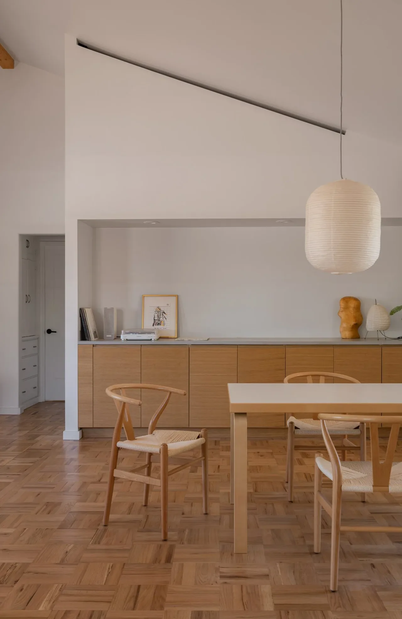 Dining area features parquet wood flooring, light wood chairs, a white rectangular table, and a hanging paper pendant light.