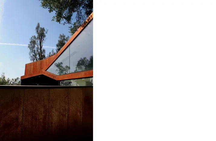 Exterior side view of a modern house featuring rust metal cladding and corner window glazing.