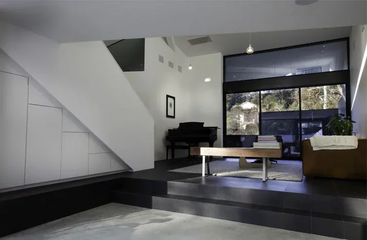 Modern living room interior with multi-level black tile flooring, large windows, and a piano in the corner.