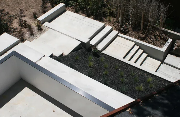Concrete terraces and stairs frame a rectangular planter in a minimal outdoor landscape design.