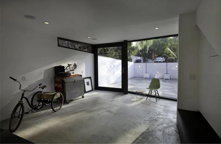 Interior view showing concrete flooring, large corner black-framed glass door and window opening to a white-walled courtyard.