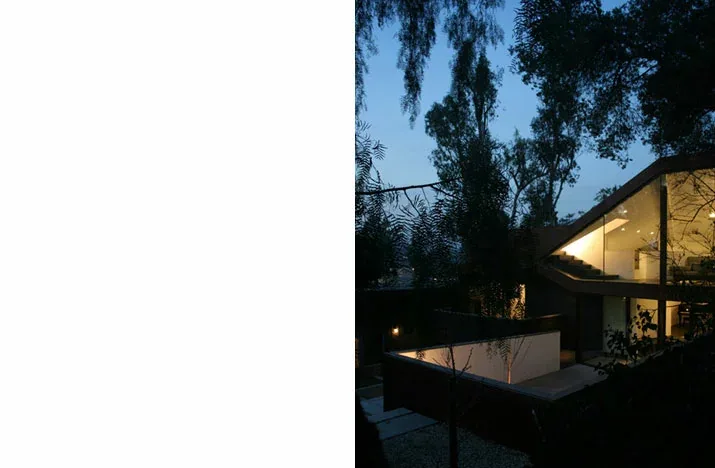 Nighttime exterior showing angled metal cladding and expansive glass facade of modern house.