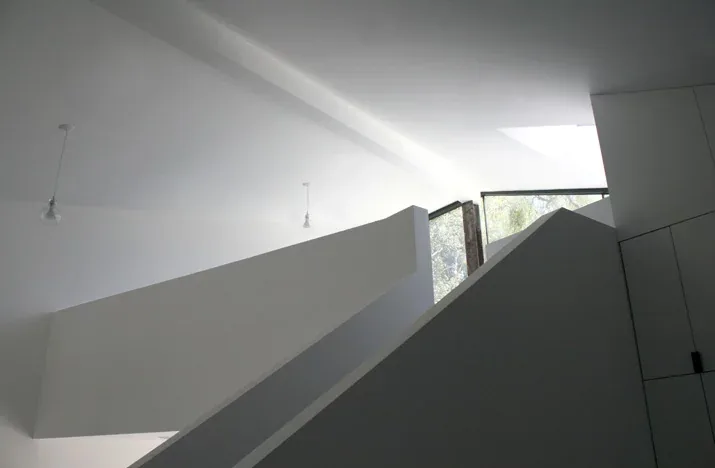 Angular white stair walls illuminated by a skylight and glass panel window in a modern interior.