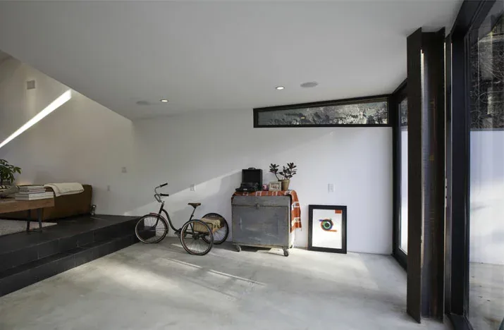 Modern living area with concrete flooring, white walls, recessed downlights, and a corner window feature.
