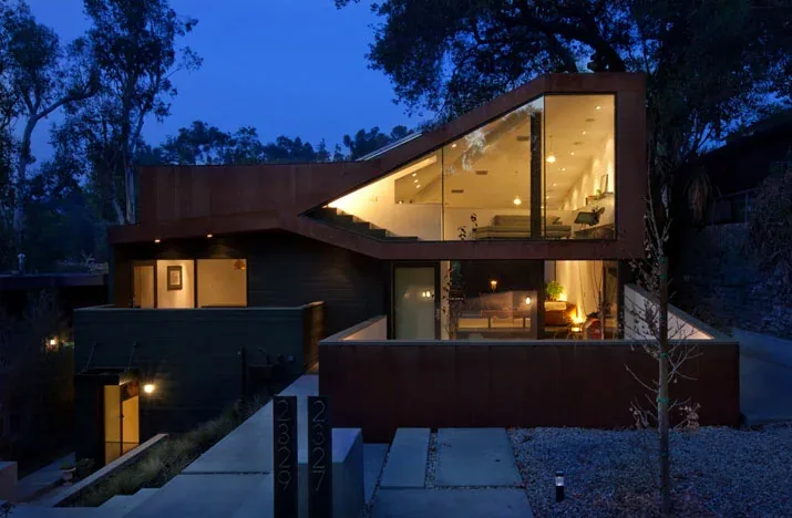 The Manifold House shows a rusted steel exterior and floor-to-ceiling glazing with angular geometry at night.
