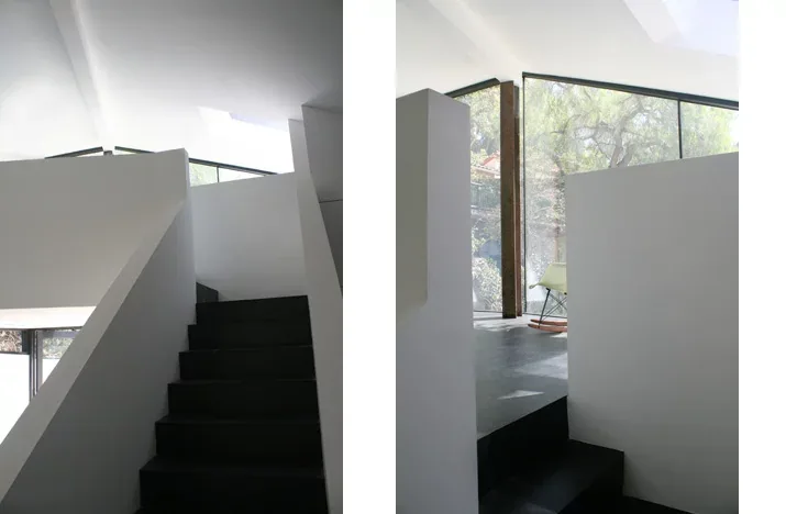 Interior stairwell with dark steps and white walls illuminated by natural light from a skylight and a large corner window.