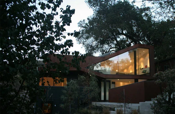 Modern two-story house with extensive floor-to-ceiling glazing and angular roof design seen in natural surroundings.