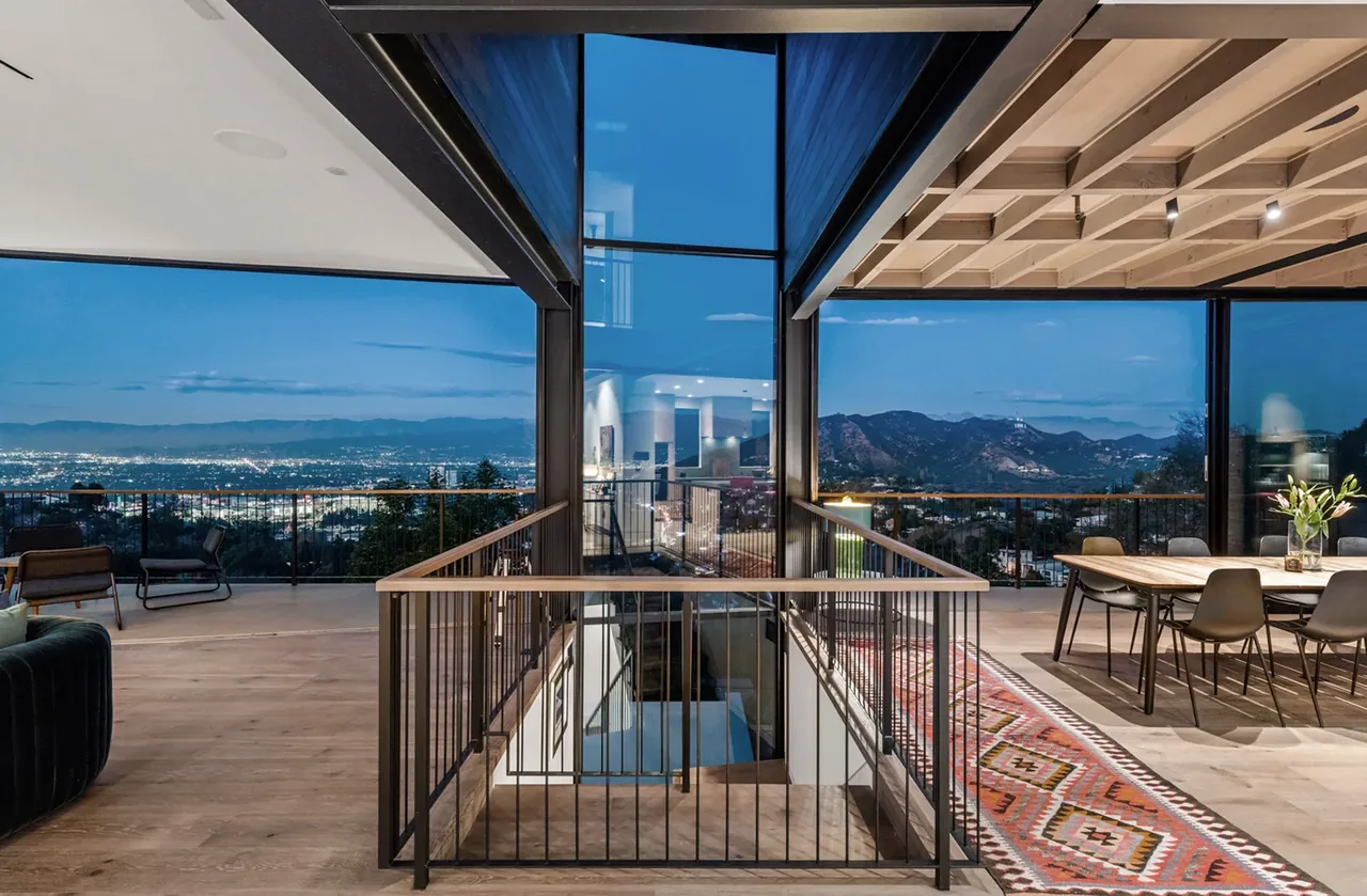 Open living and dining area with glass walls overlooking city and mountain views at dusk.