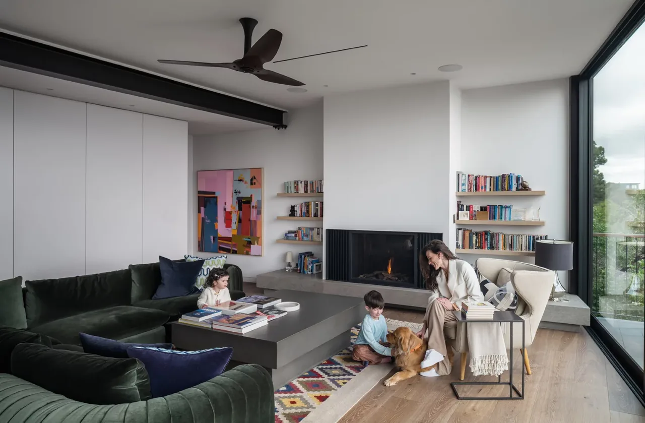 Living room featuring a fireplace flanked by built-in bookshelves and floor-to-ceiling glazing providing natural light.
