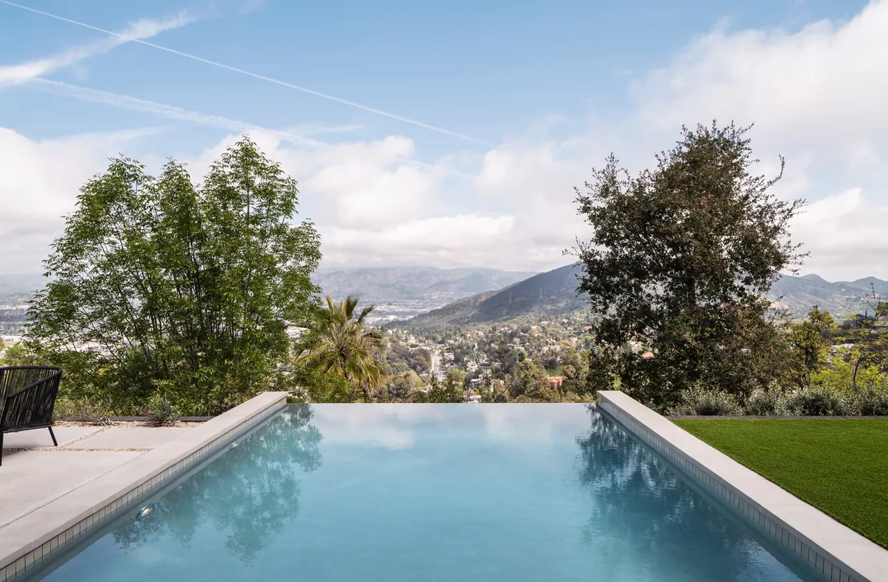 Infinity edge swimming pool with surrounding landscaping and distant mountain view.