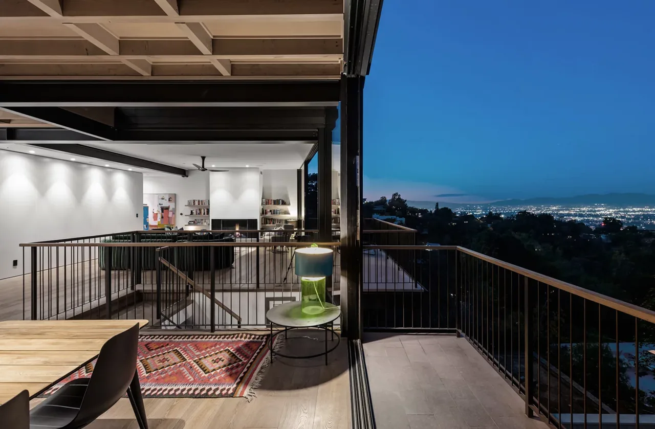 Interior living room with coffered ceiling opening to a terrace overlooking cityscape at dusk.