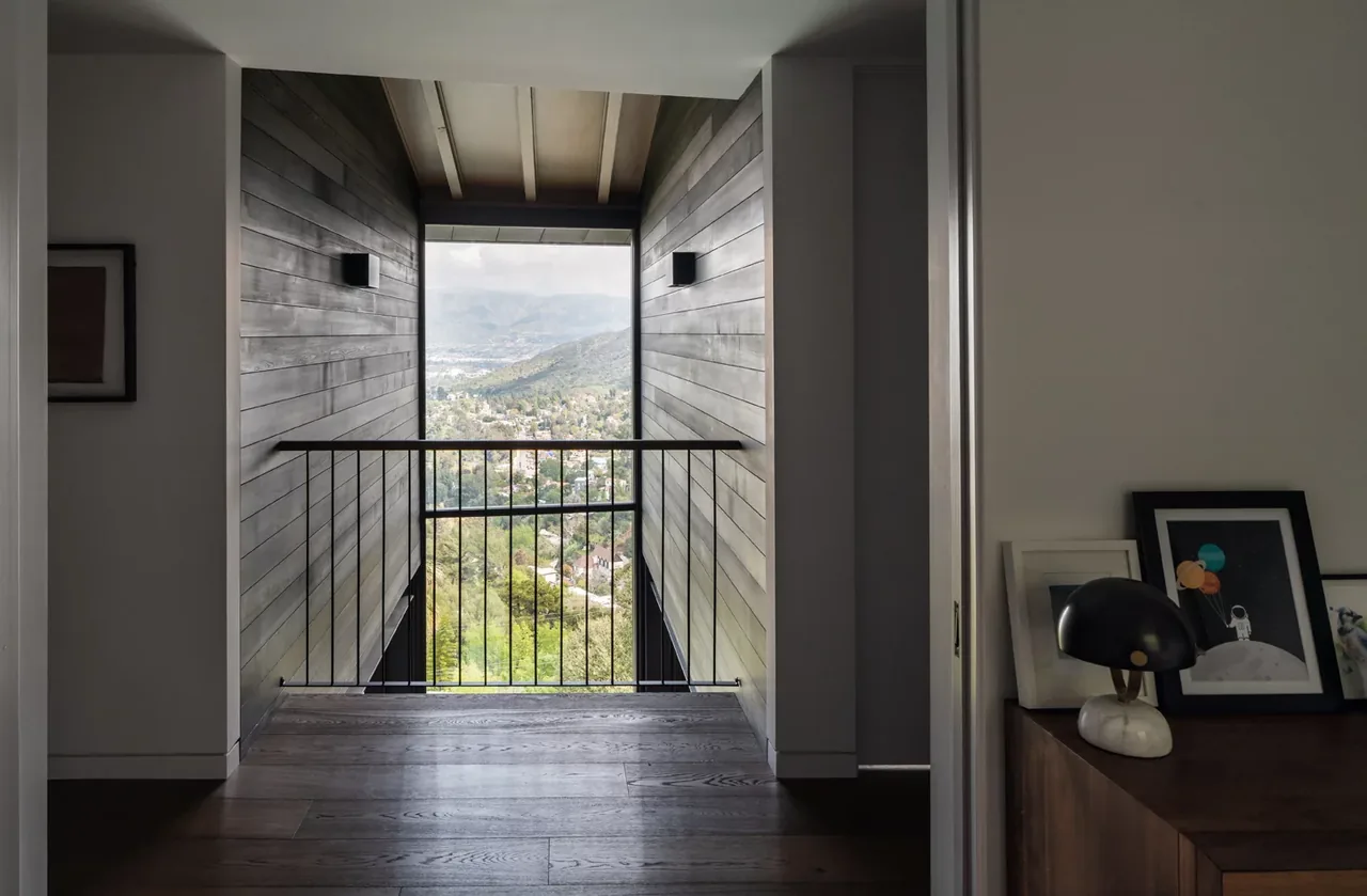 A hallway with wood-paneled walls and metal railing opening to a view of a green valley.