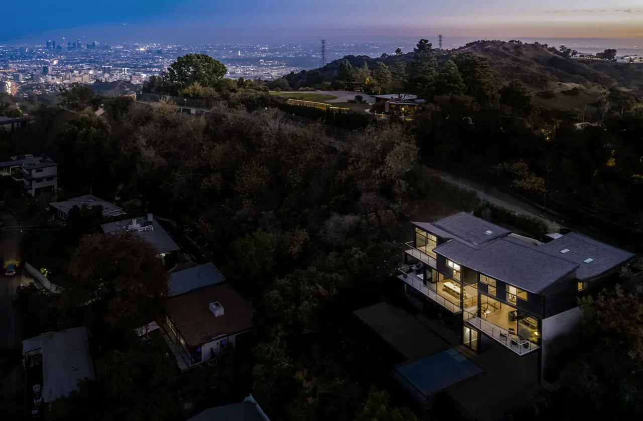 Night aerial photo of a hillside residence featuring large glass walls and outdoor balconies overlooking the city.