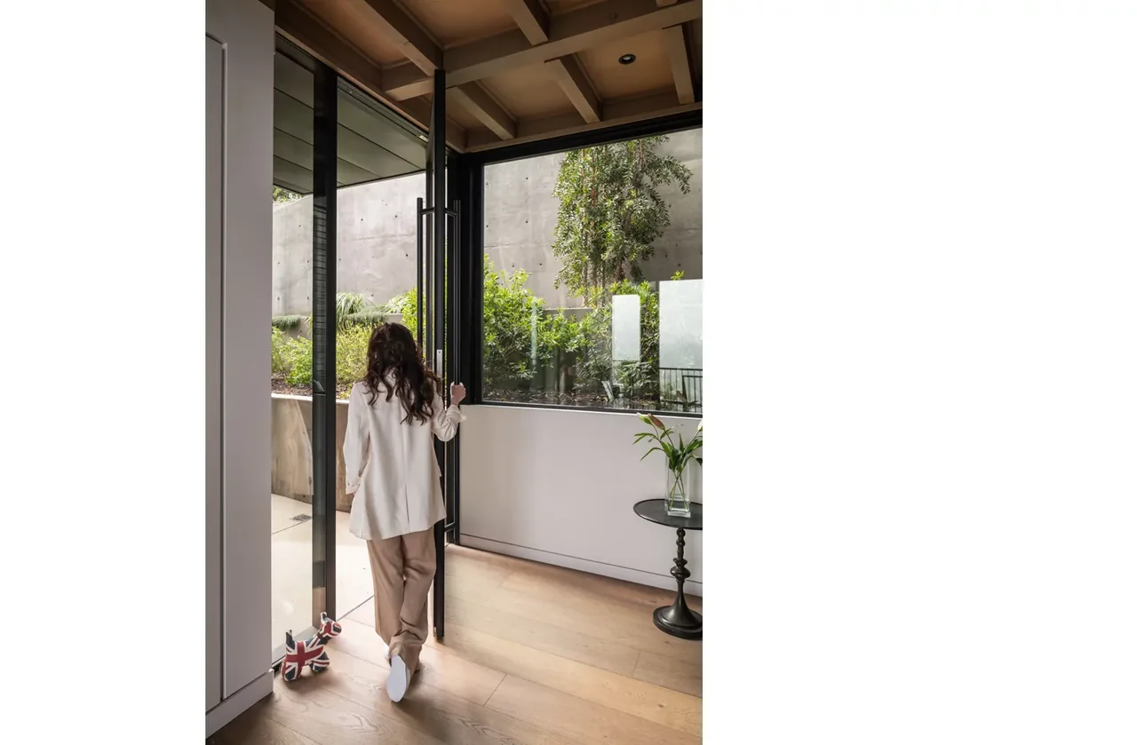 Interior view showing a pivot door opening to an outdoor area with concrete walls and vegetation.