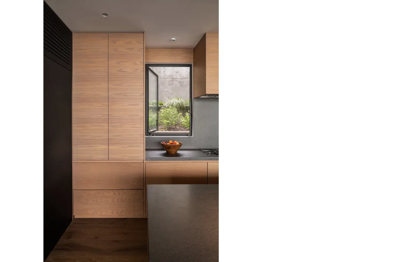 A kitchen featuring wood cabinetry and a countertop with a bowl of fruit next to a small open window.
