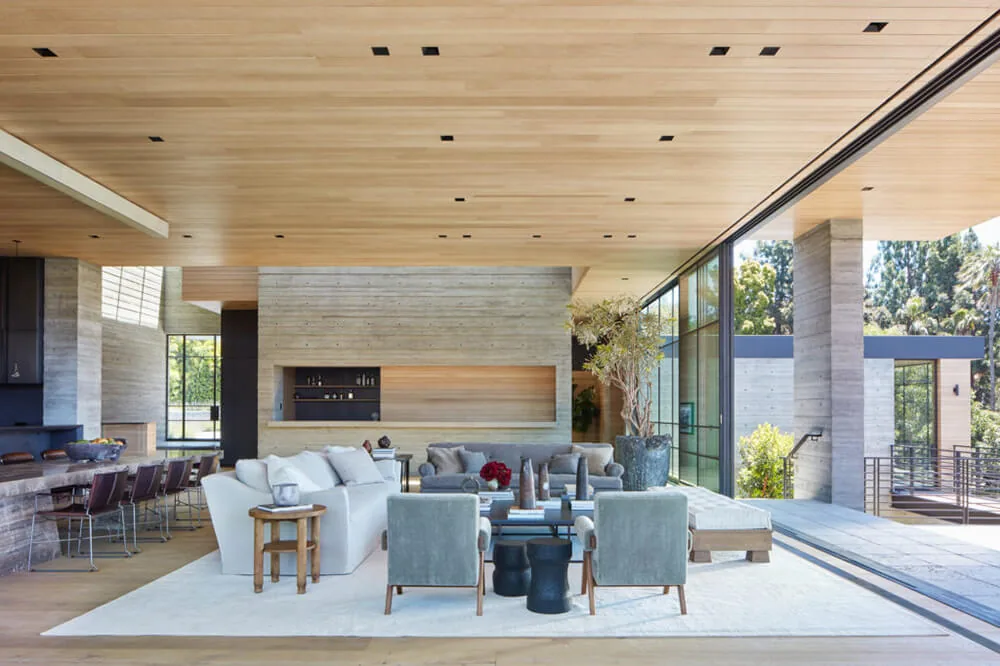 Interior view of the Sapire Residence living room featuring wood ceiling, concrete wall, and floor-to-ceiling glass doors.