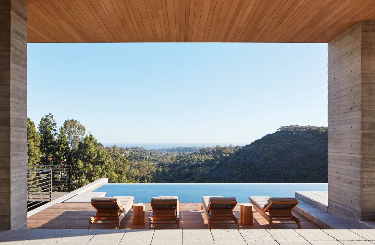 Covered patio overlooking a rectangular infinity pool with wooden lounge chairs and distant mountain views at Sapire Residence.