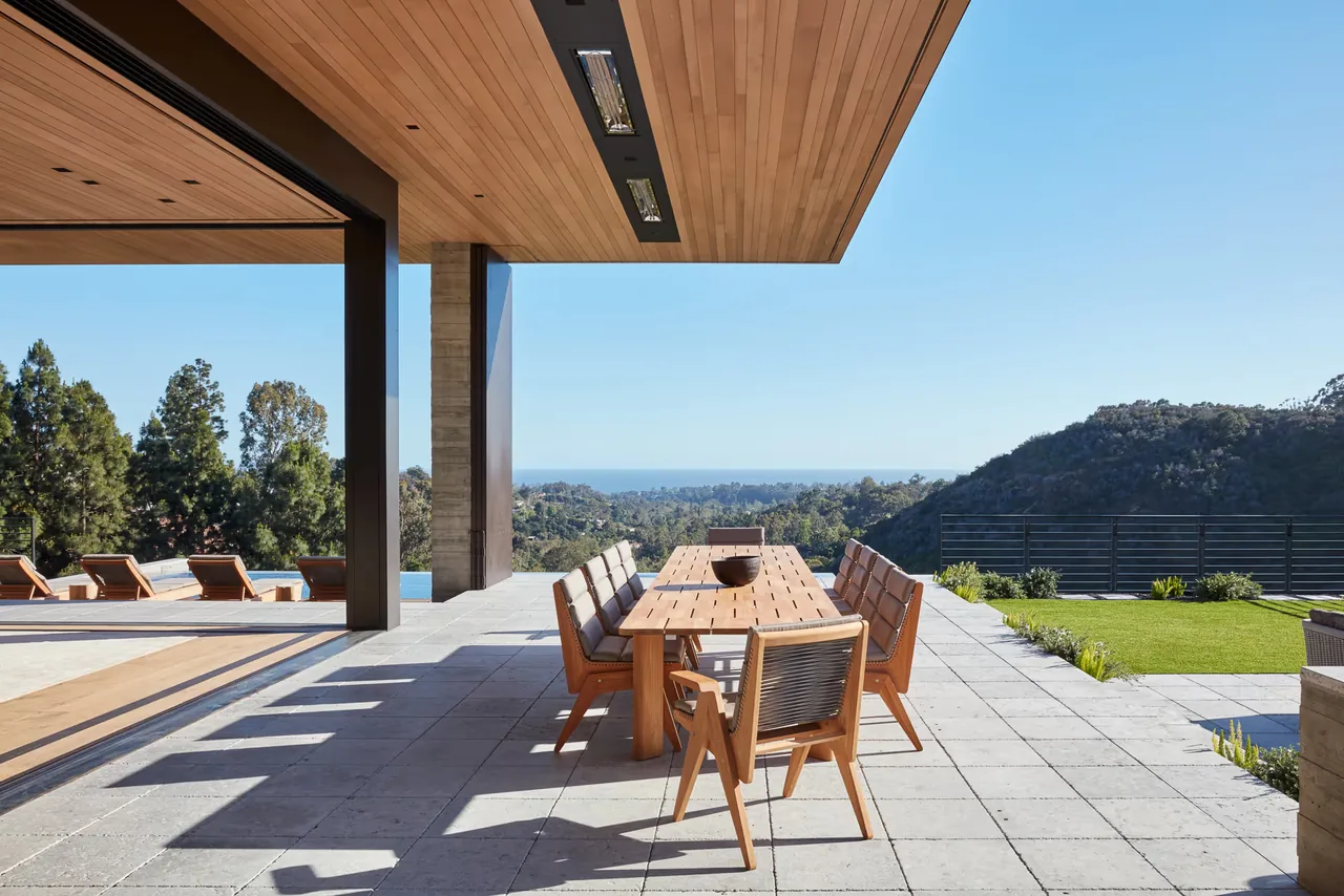 The Sapire Residence features an open patio with a wooden dining table, mountain views, and an infinity pool in Los Angeles.