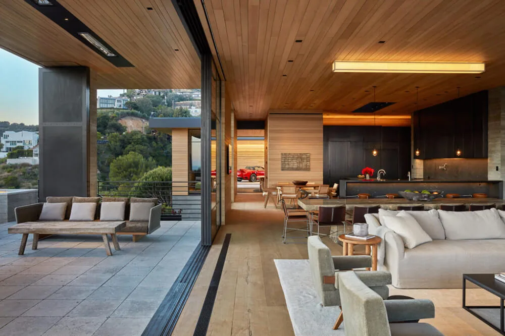 The Sapire Residence by Abramson Houses features indoor-outdoor flow with wood plank ceilings and a modern kitchen visible from the living area.