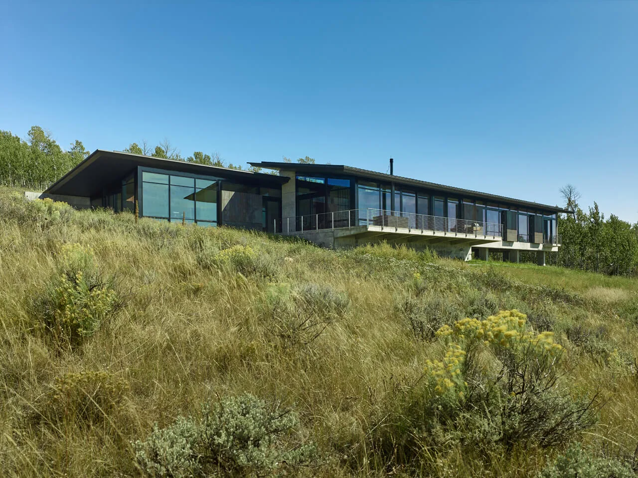 Wyoming Residence features a long horizontal facade with extensive glass walls and a black sloping roof adapting to a sloping site.