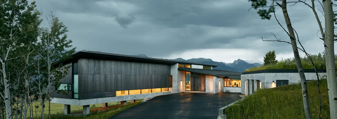 Wyoming Residence features a long horizontal facade with a sloping black roof and grass-covered roof areas integrating into the landscape.
