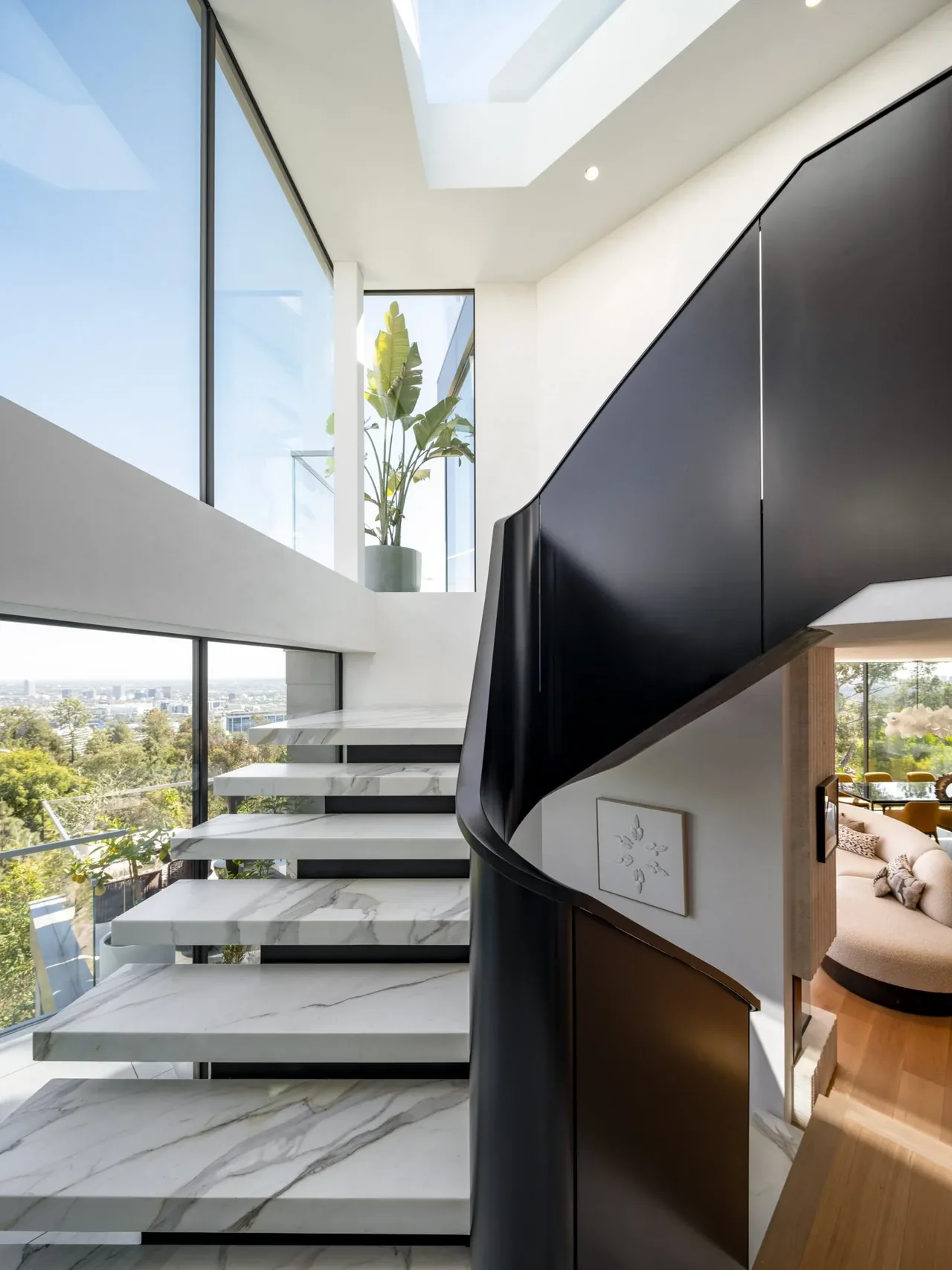 Interior view of a curved floating marble staircase with a black balustrade and floor-to-ceiling glazing.