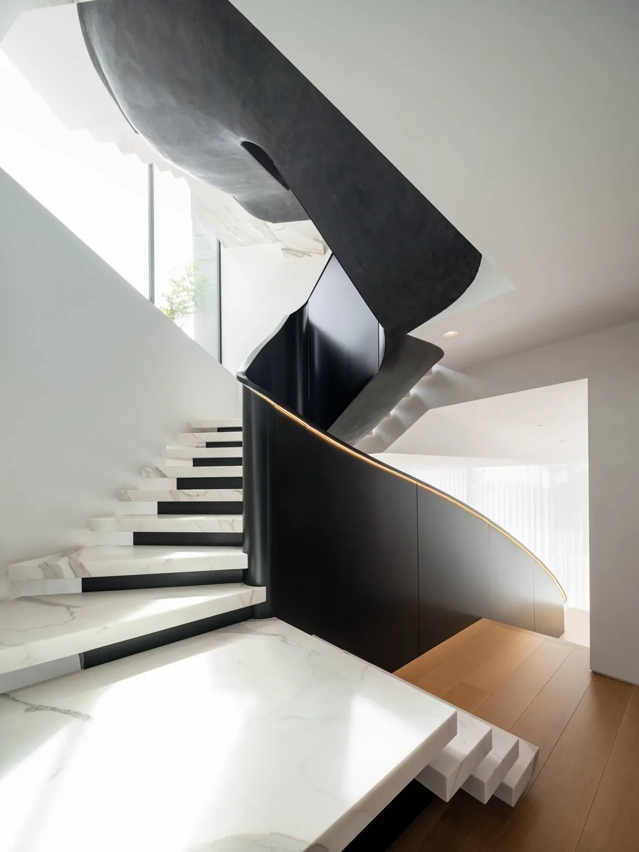 Curved staircase with white marble floating steps and a black curved balustrade with integrated lighting in a modern interior space.
