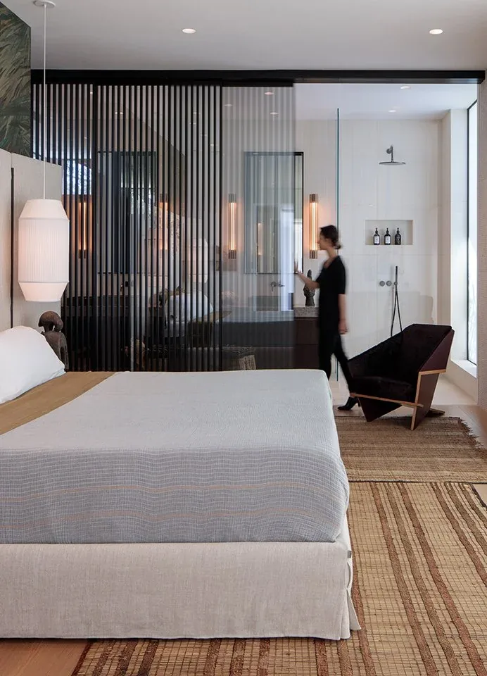 Bedroom with a partially visible bathroom separated by vertical black slatted partition and glass.