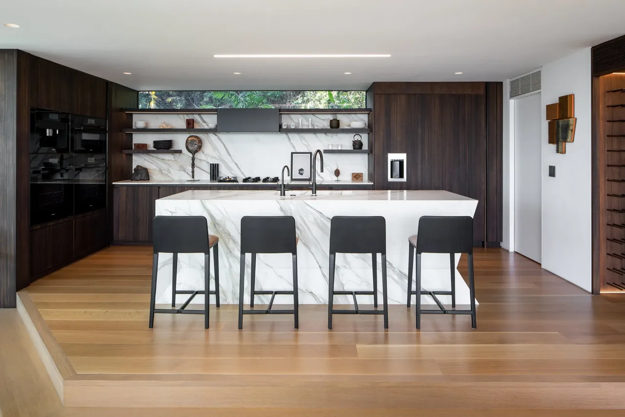 Kitchen with marble island, dark wood cabinets, open shelving, and integrated appliances.