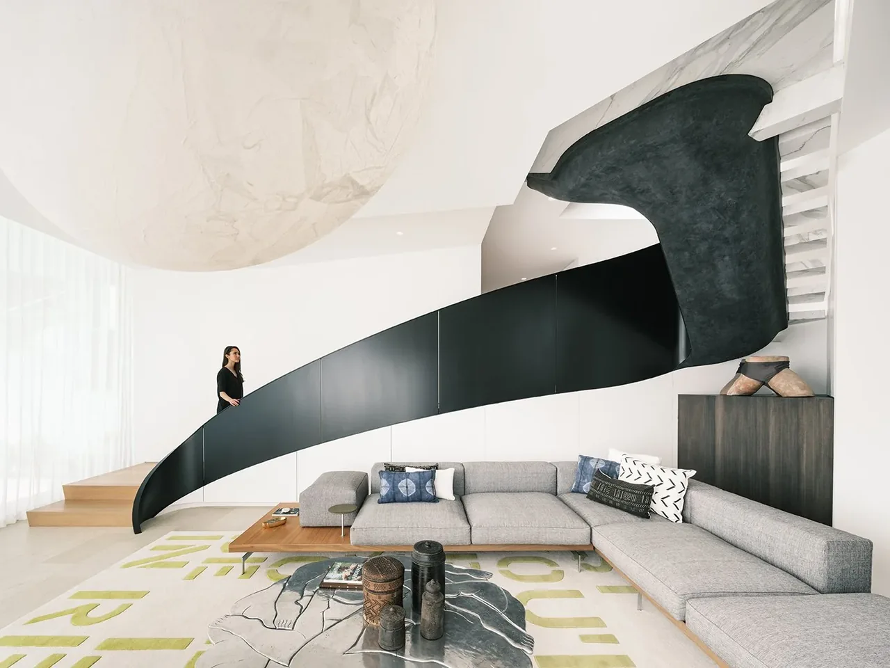 Interior of a modern living room featuring a distinctive curved black staircase and contemporary furnishings.