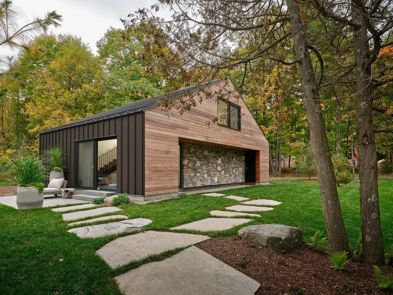 Muskoka Cottage features wood and stone siding with a gable roof set in an autumnal wooded landscape.