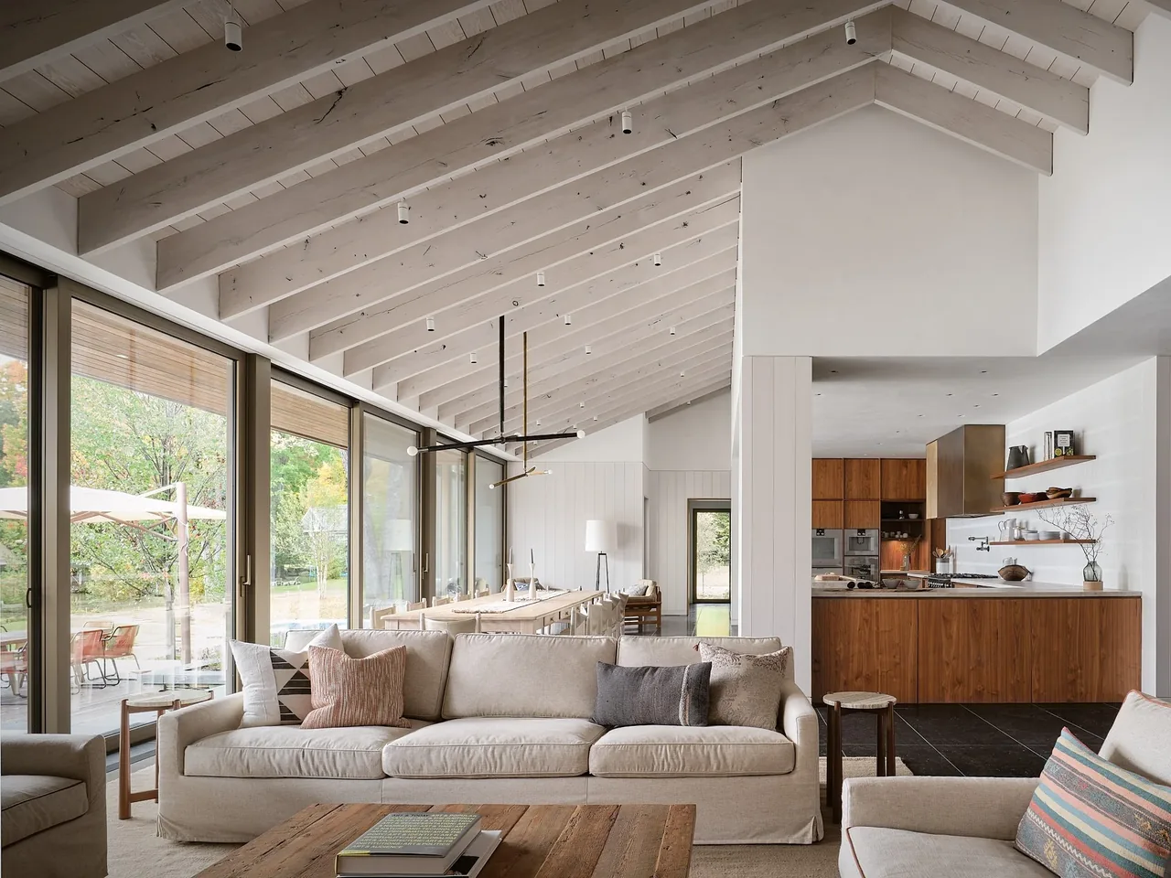 The Muskoka Cottage features a vaulted ceiling living room opening to a kitchen with wood cabinetry and large glass windows.