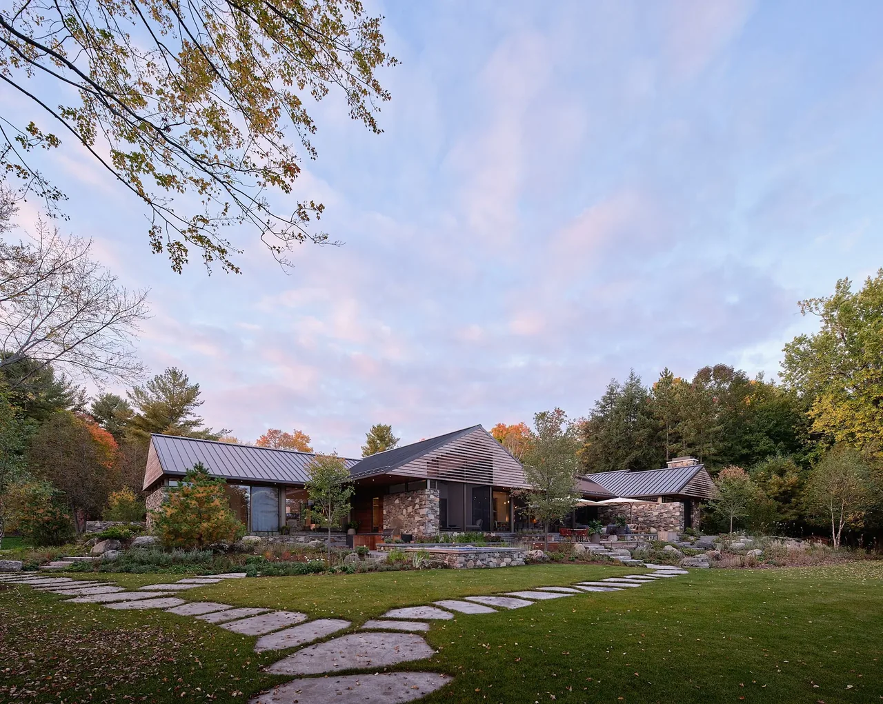 Muskoka Cottage features stone exterior walls and a standing seam metal gable roof with a landscaped garden and stone walkway.
