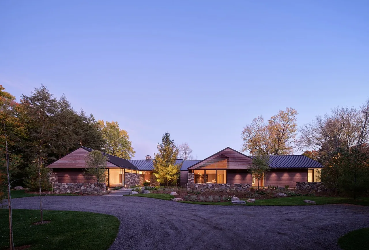 The Muskoka Cottage features dark wood siding, stone wall accents, and a metal gable roof, creating a harmonious natural setting.