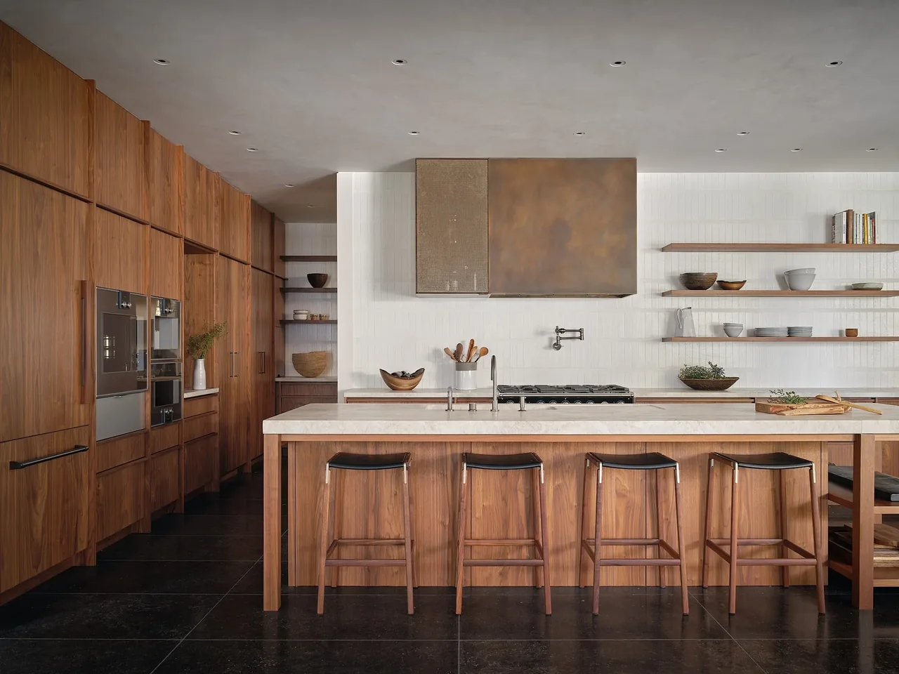The Muskoka Cottage kitchen features walnut cabinetry, black floor tiles, and open wood shelving with a metal range hood.