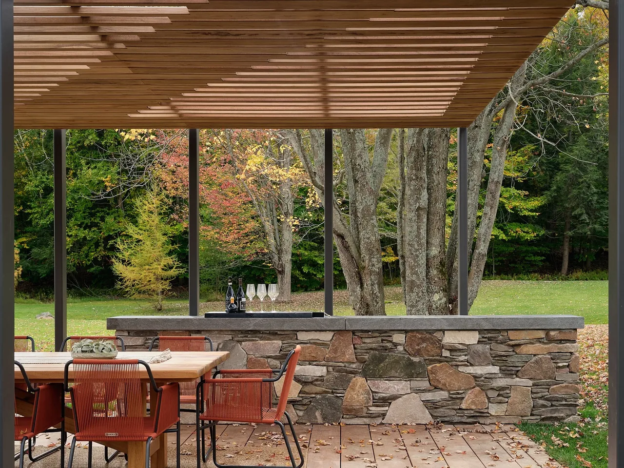 Covered outdoor dining space featuring a wooden slatted pergola roof and a stone bar counter at Muskoka Cottage.