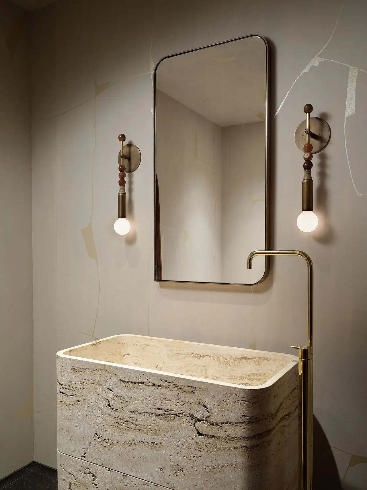 Bathroom with a stone vessel sink, brass faucet, a tall mirror, and decorative brass wall sconces with globe bulbs.